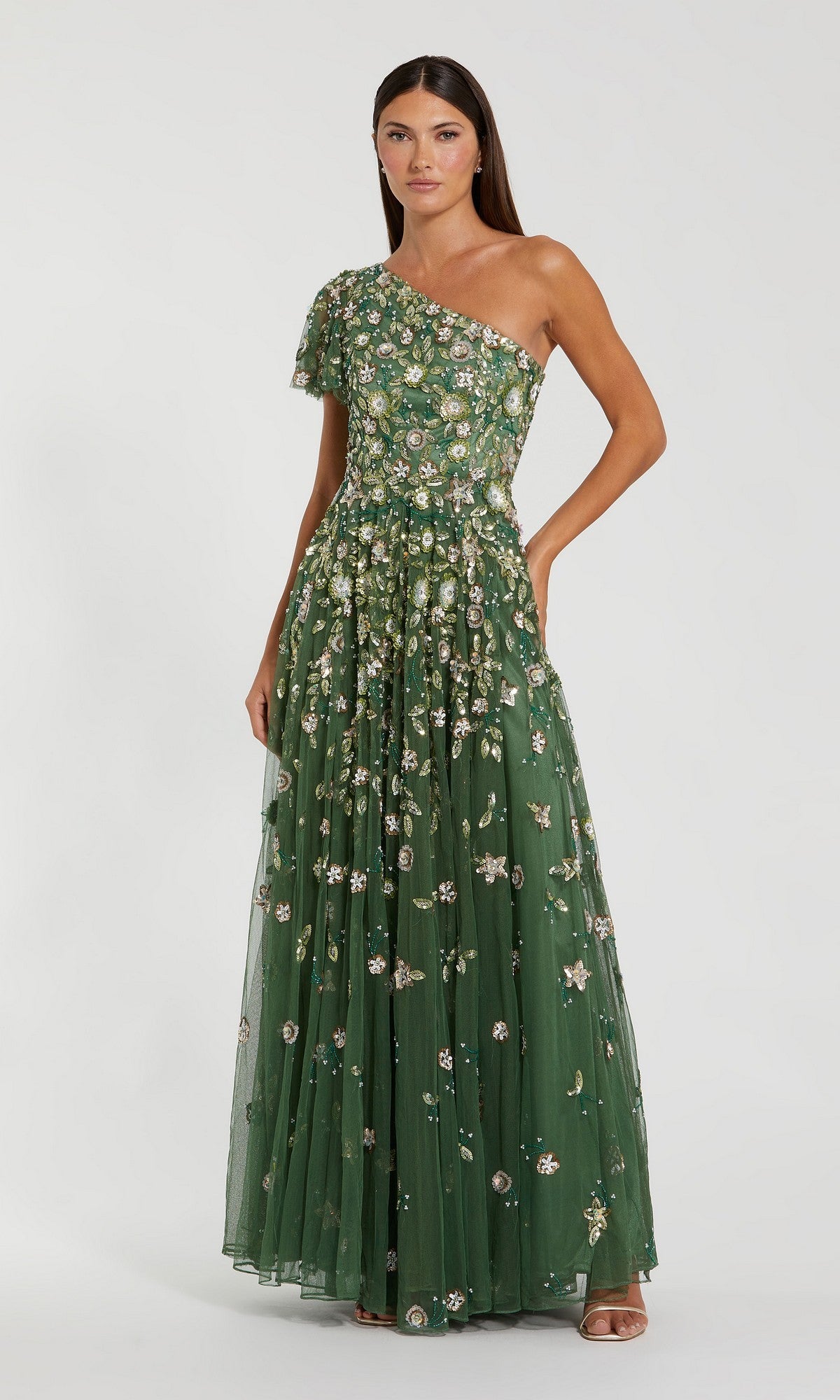 A woman wearing the Mac Duggal 6159 long formal dress in sage stands against a neutral background. The elegant gown features a sophisticated one-shoulder design, delicate floral embellishments, and a floor-length silhouette, making it ideal for special occasions.